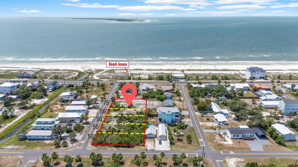 Aerial view of a marked vacant lot near the beach, with the shoreline and beach access visible beyond the neighborhood.
