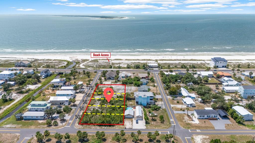 Aerial view of a marked vacant coastal lot near homes, with beach access and the Gulf beyond.