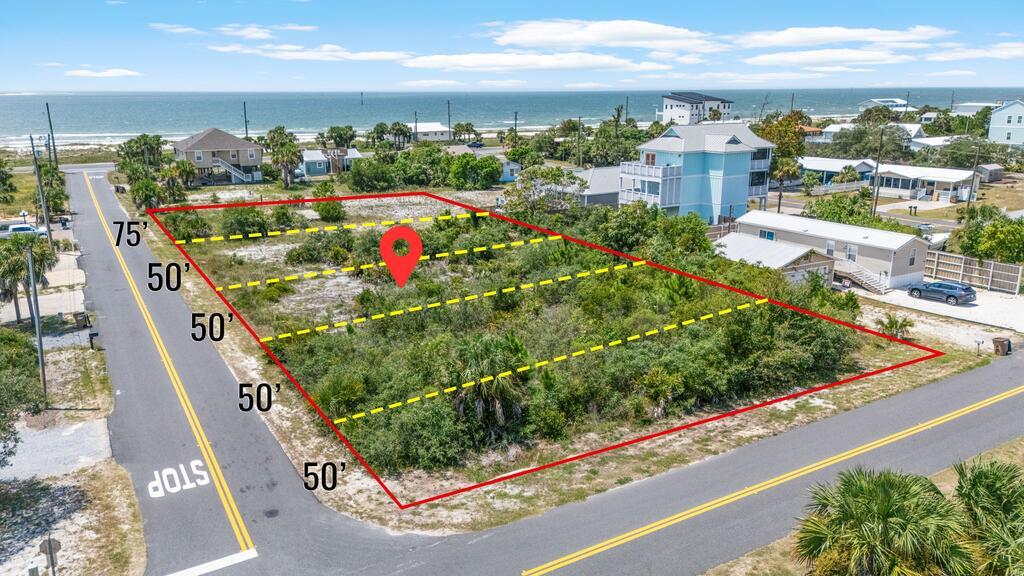 Aerial view of a marked vacant lot near the Gulf, with neighboring homes and shoreline beyond.