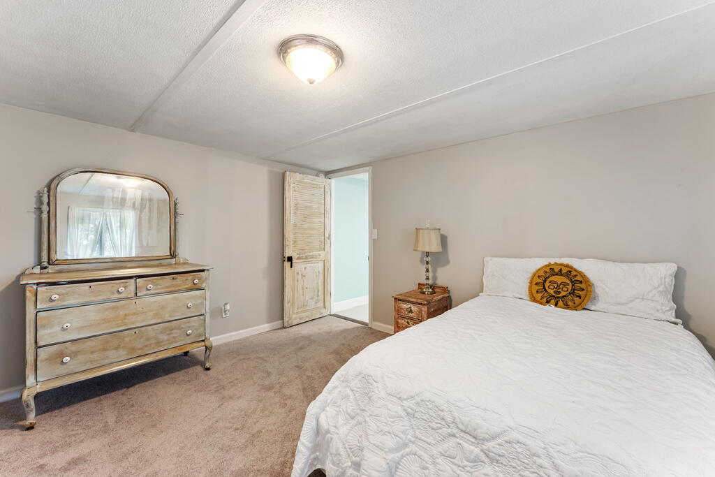 Bedroom with a white bed, beige carpet, and distressed wood dresser with mirror.