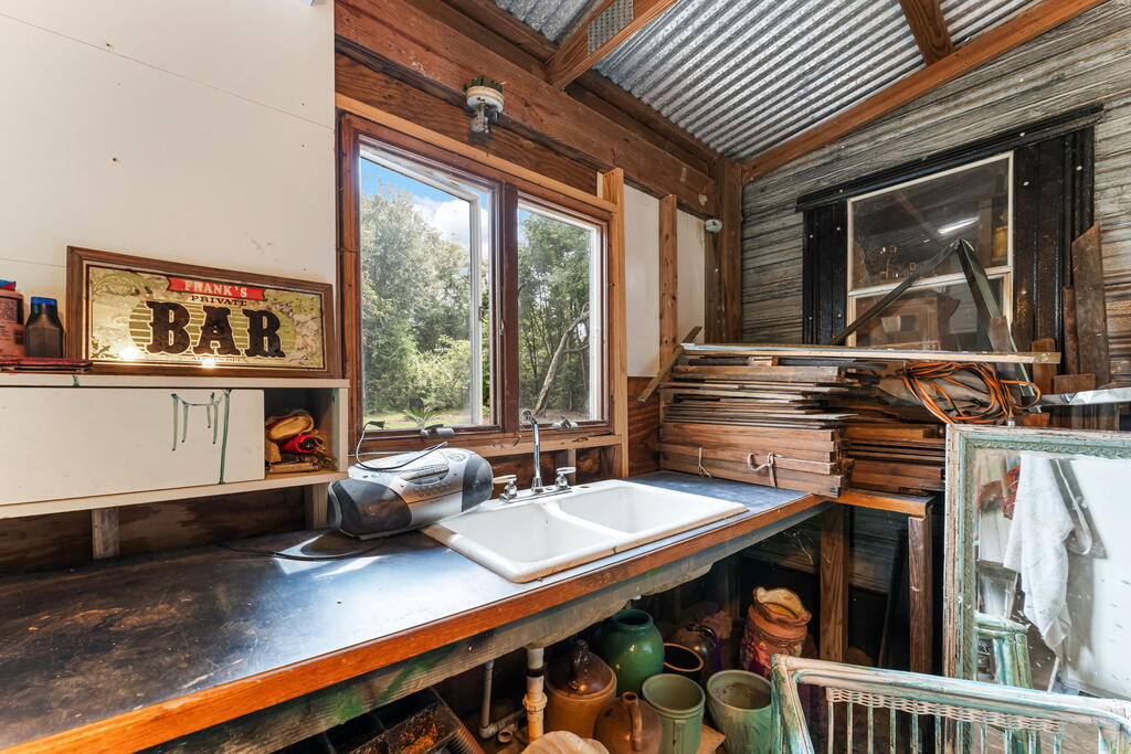 Rustic workroom with a white sink, metal counter, exposed wood framing, and corrugated metal ceiling.