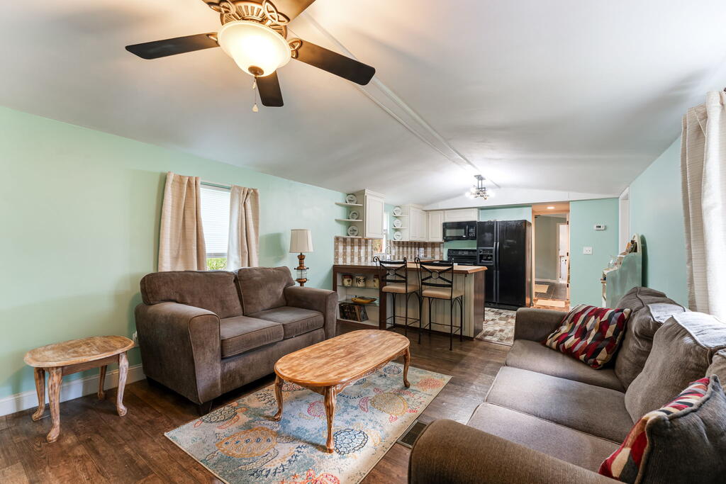 Living room with brown sofas and a patterned rug, opening to a kitchen with a breakfast bar.
