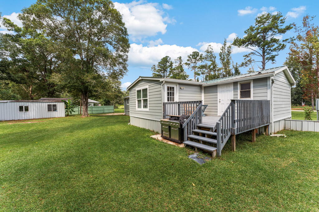Light-gray manufactured home with a raised deck and grill beside a broad grassy yard.