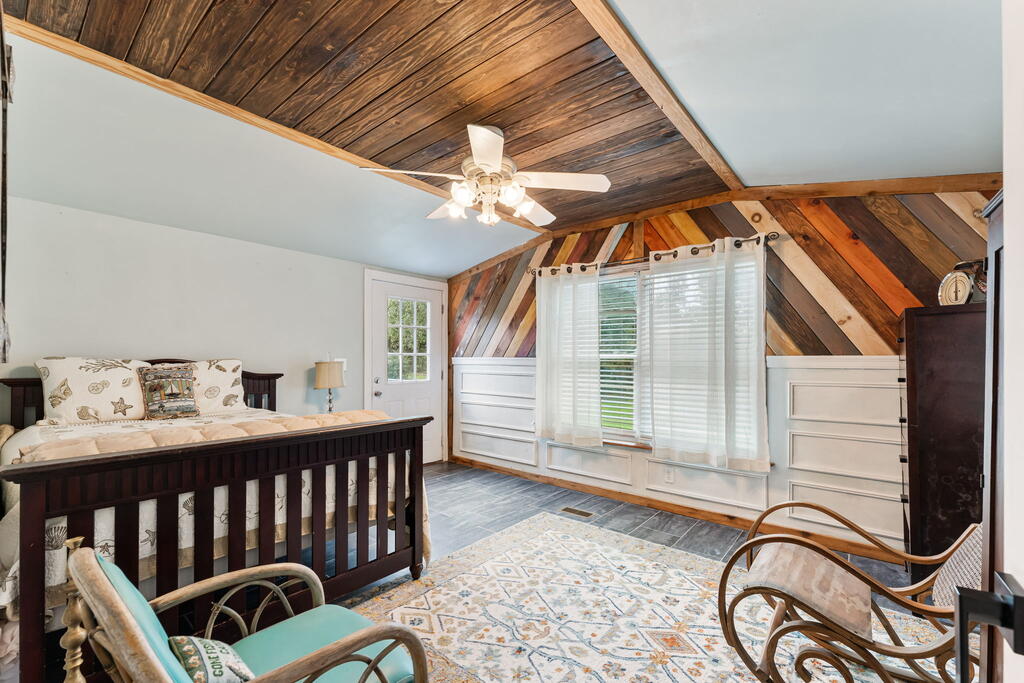 Bedroom with a dark wood bed, patterned rug, and wood-plank vaulted ceiling.