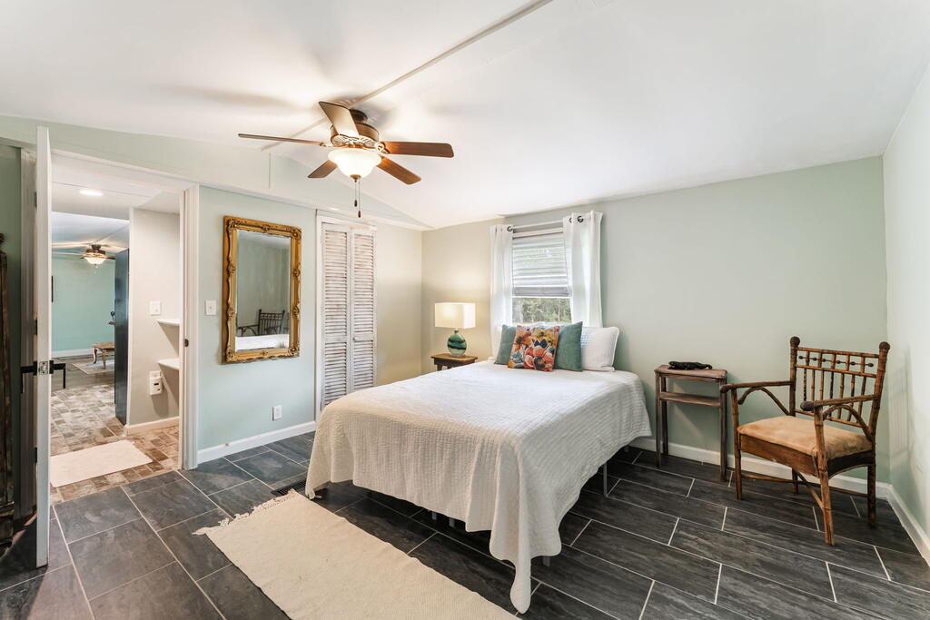 Bedroom with a white-covered bed, dark tile flooring, and ceiling fan.