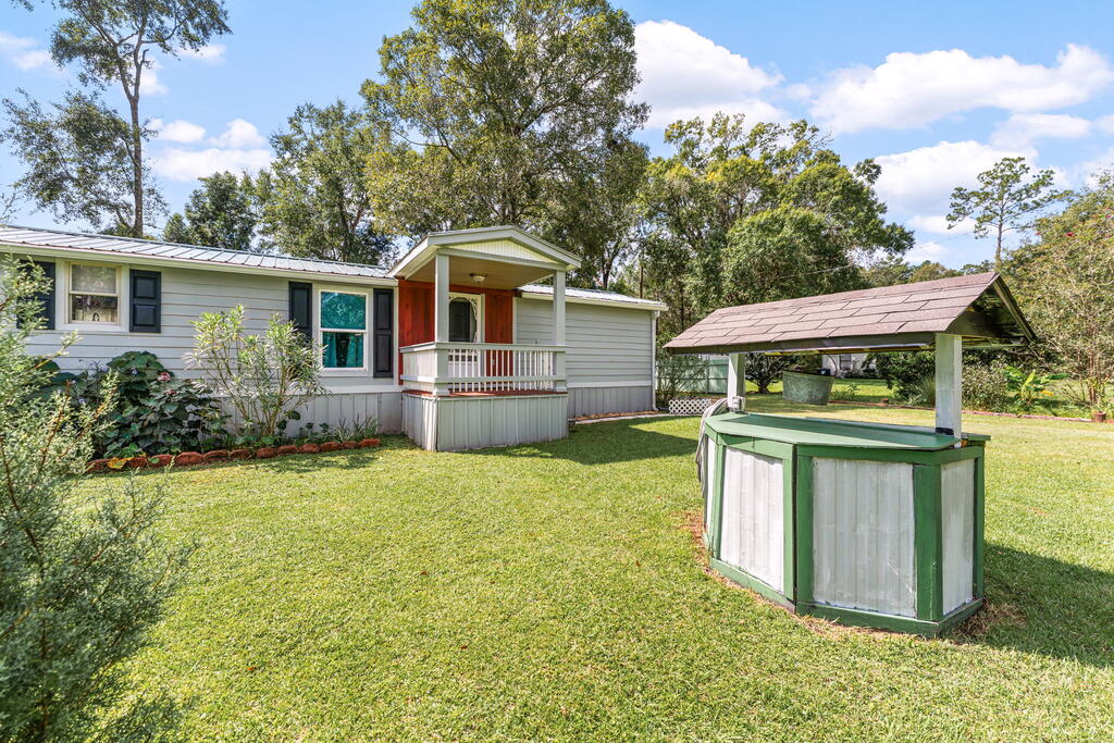 Manufactured home with a covered porch and a roofed well structure in the grassy yard.
