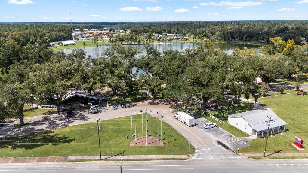Aerial view of a tree-lined lakeside property with buildings, parking areas, and a flag plaza.