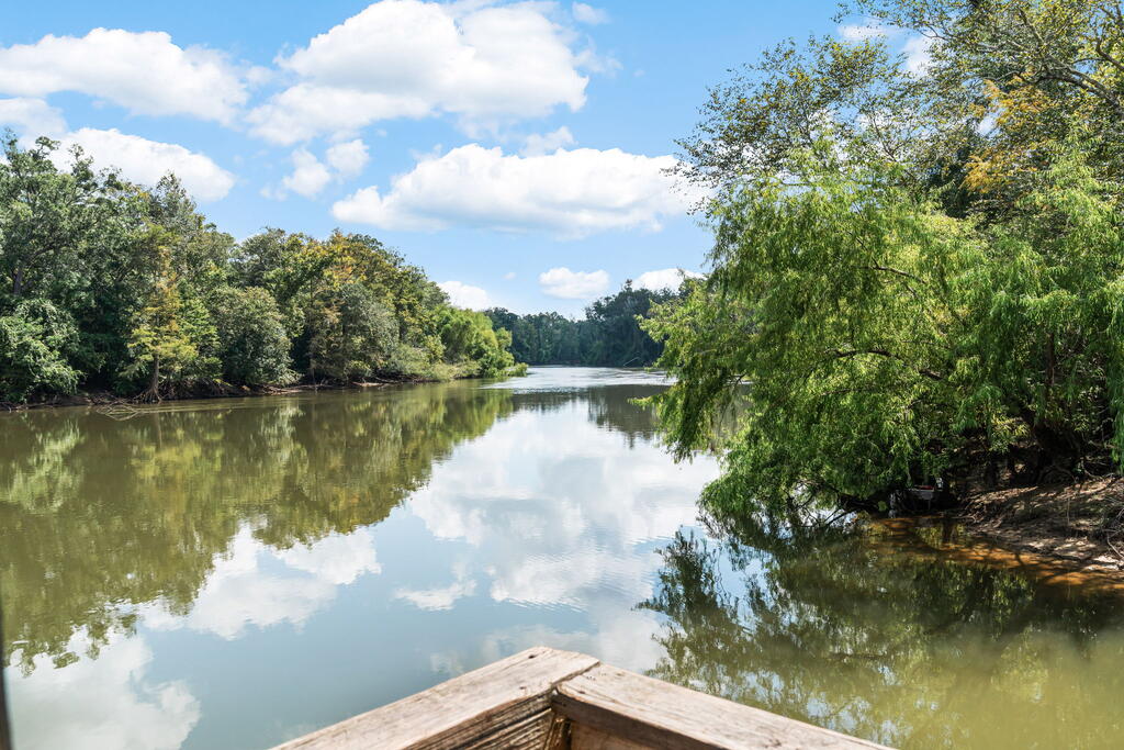River and wooded banks viewed from a wooden dock, with clouds reflected in the calm water.