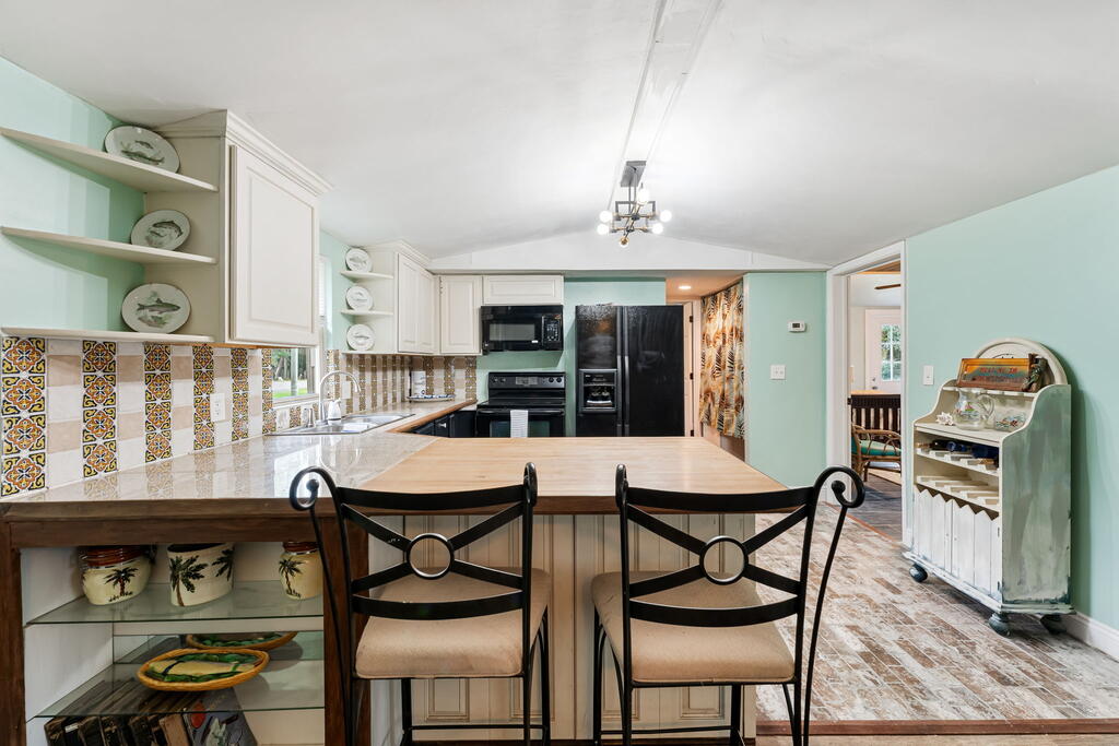 Kitchen and dining area with a wood island, mint-green walls, patterned tile backsplash, and black appliances.