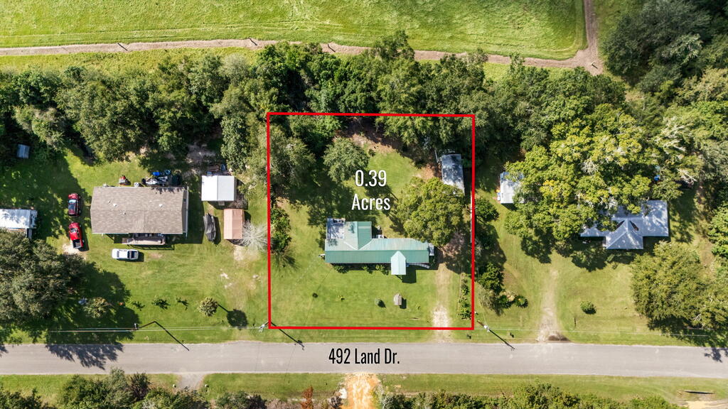 Aerial view of a tree-lined 0.39-acre lot, outlined in red, with a house beside the road.