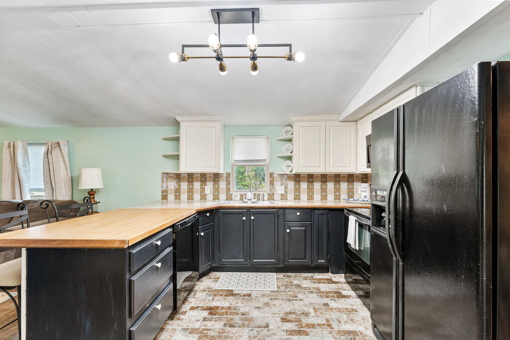 Kitchen with black cabinets, a long butcher-block island, and a patterned tile backsplash.