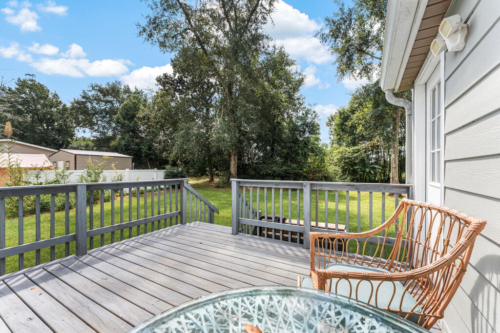 Wooden deck with wicker chairs overlooking a green yard and mature trees.
