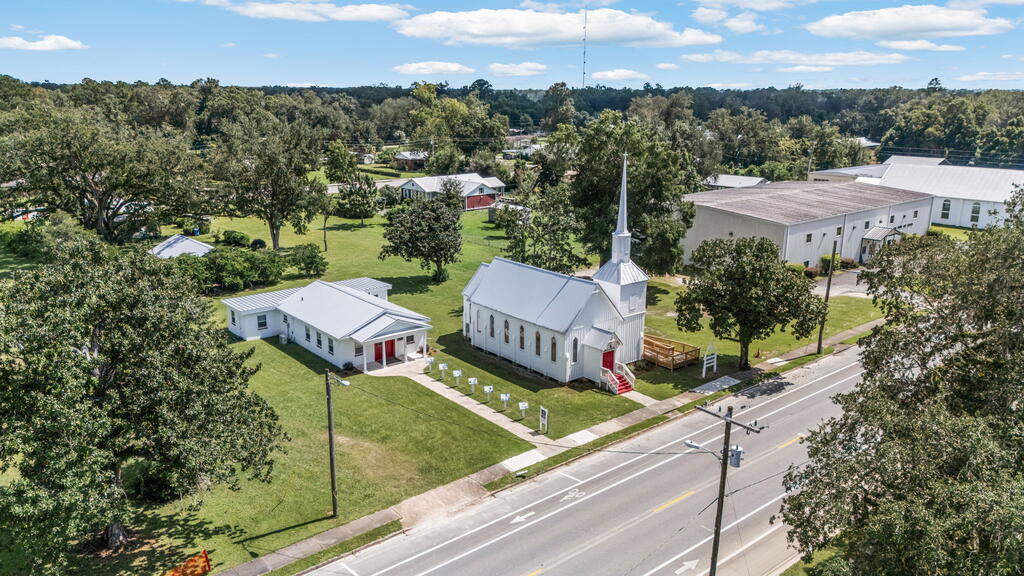 Aerial view of a white church with a tall steeple beside a two-lane road.