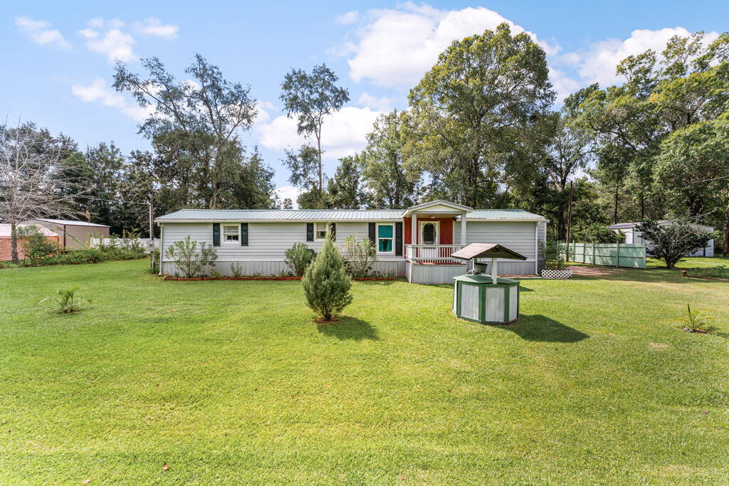Single-story home with a covered porch, broad lawn, mature trees, and a small roofed garden feature.