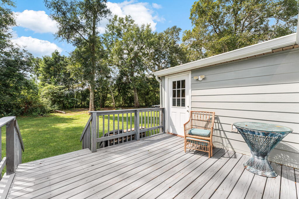 Furnished wooden deck beside a gray-sided home, overlooking a tree-lined lawn.