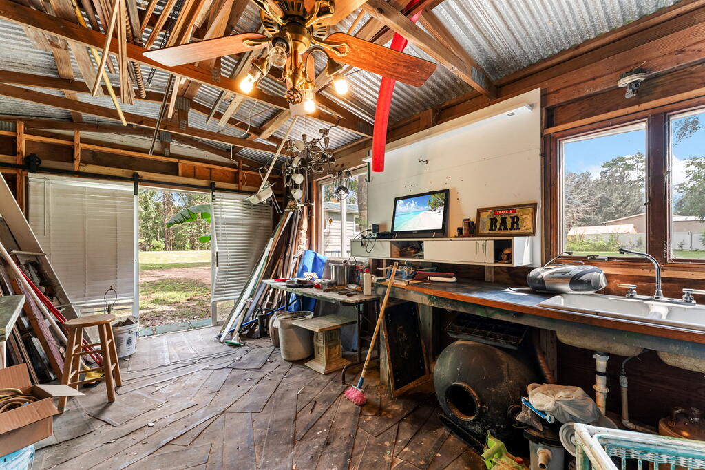 Workshop with exposed beams, a corrugated metal ceiling, crowded workbenches, and a long sink.
