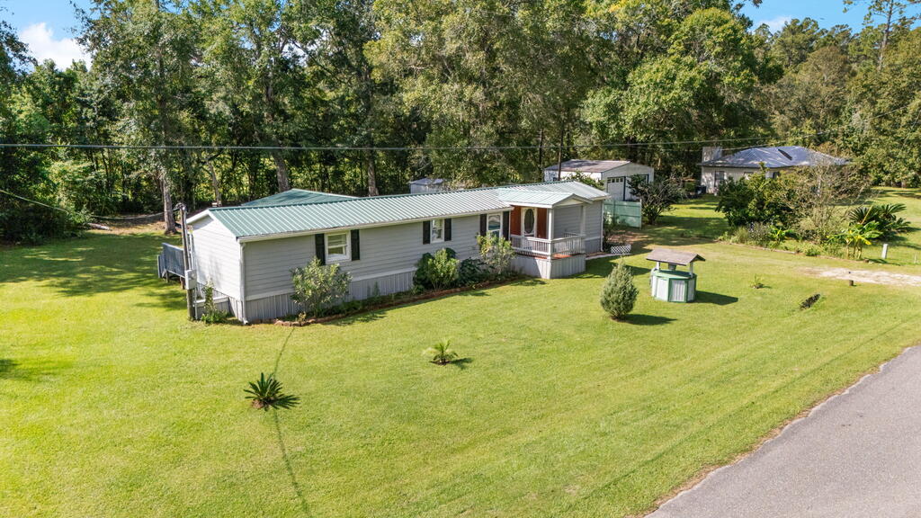 Aerial view of a single-story home with a green metal roof, broad lawn, and wooded surroundings.