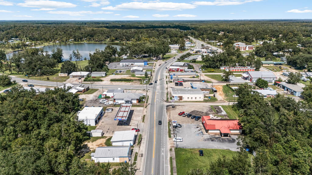 Aerial view of a town with a central road, commercial buildings, a lake, and surrounding woods.
