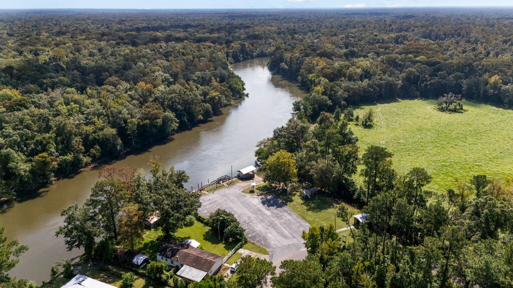 Aerial view of a wooded riverfront property with a grassy clearing and paved parking area.