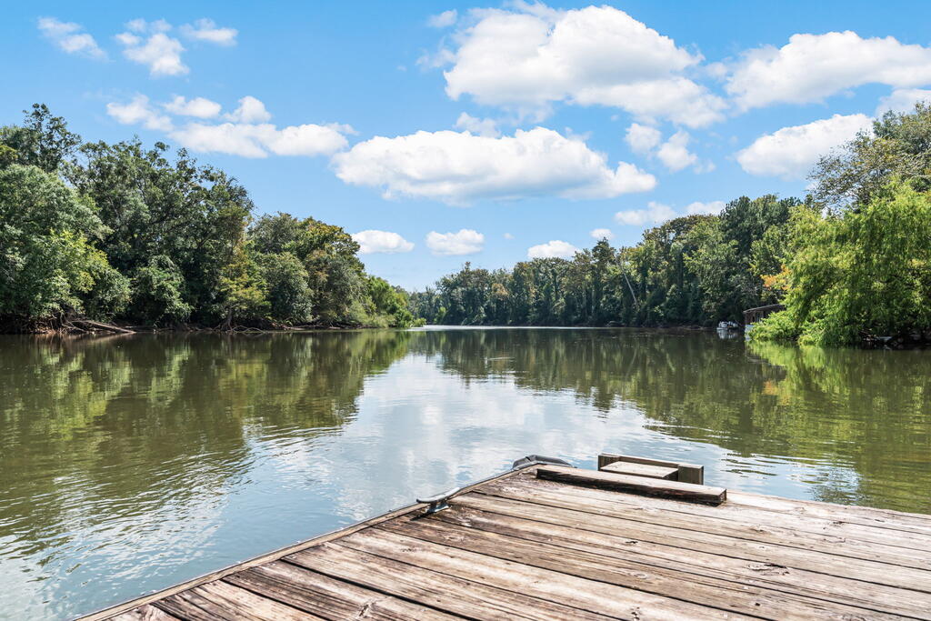 Wooden dock overlooks a calm, tree-lined river beneath a partly cloudy sky.