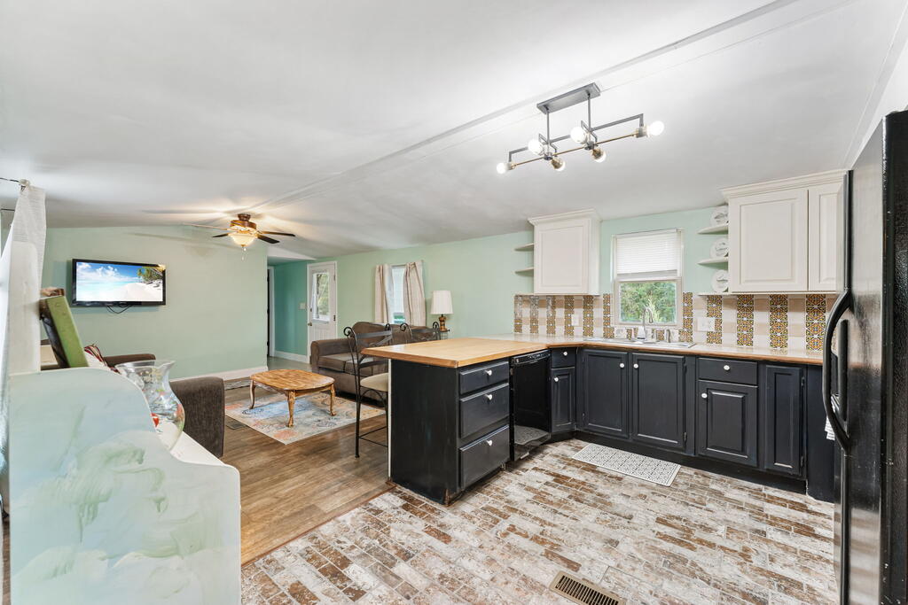 Open kitchen with black cabinets, a wood-topped island, patterned backsplash, and adjoining living area.
