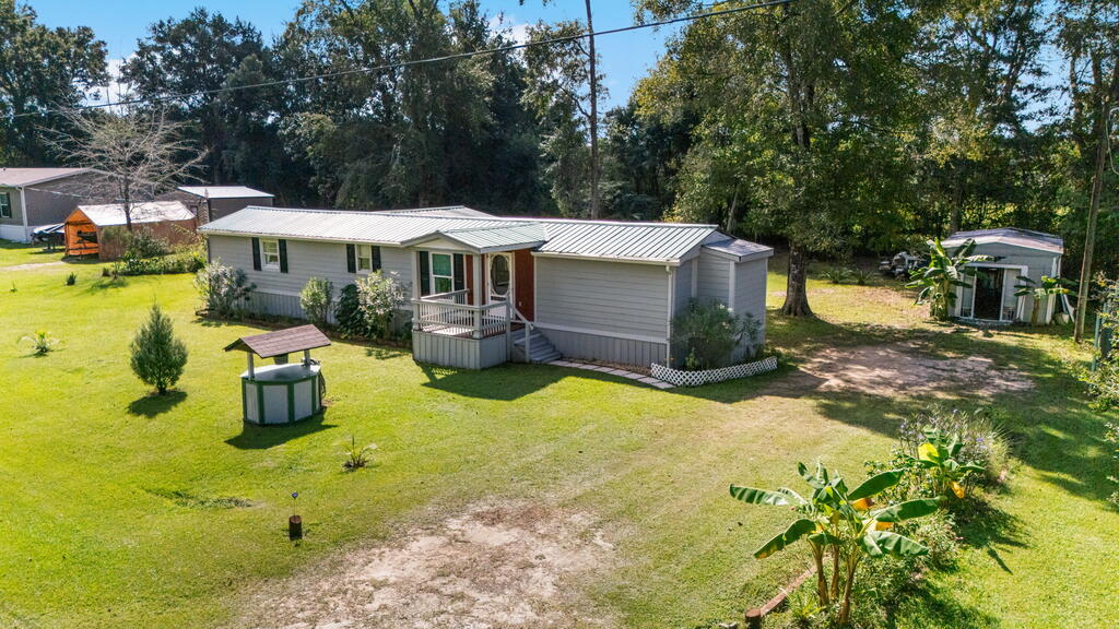 Gray manufactured home with a metal roof and front porch in a broad grassy yard.