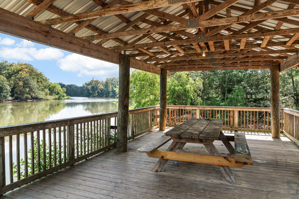 Covered wooden deck with a picnic table overlooking a calm, tree-lined river.