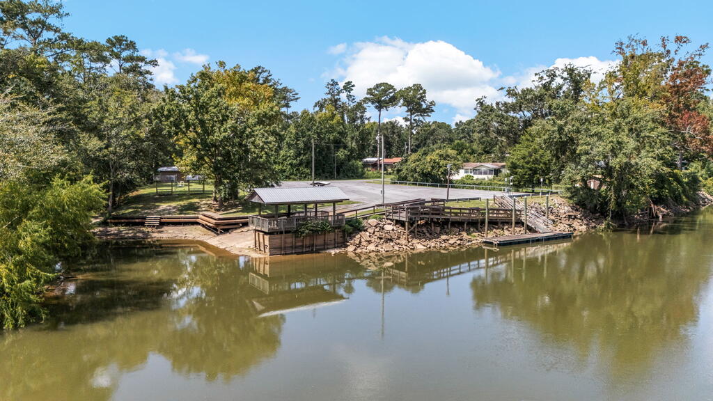 Waterfront property with a covered dock, wooden shoreline walkways, and a paved area among trees.