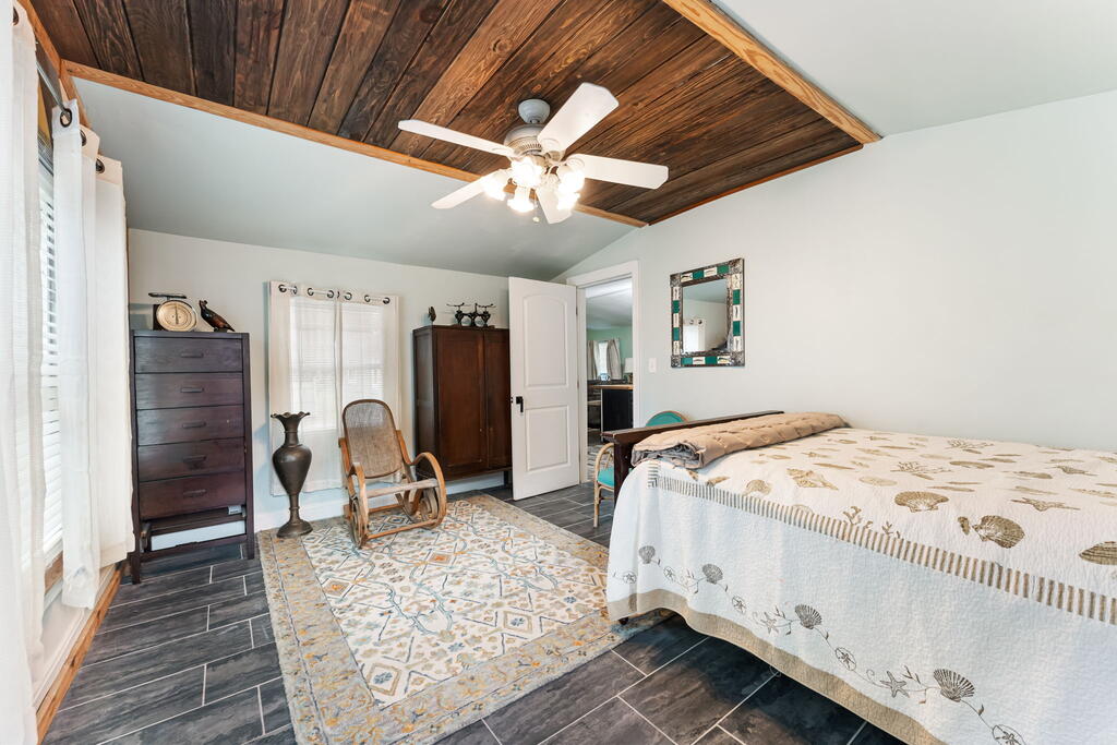 Bedroom with a seashell-patterned bedspread, rocking chair, and dark wood-plank ceiling.