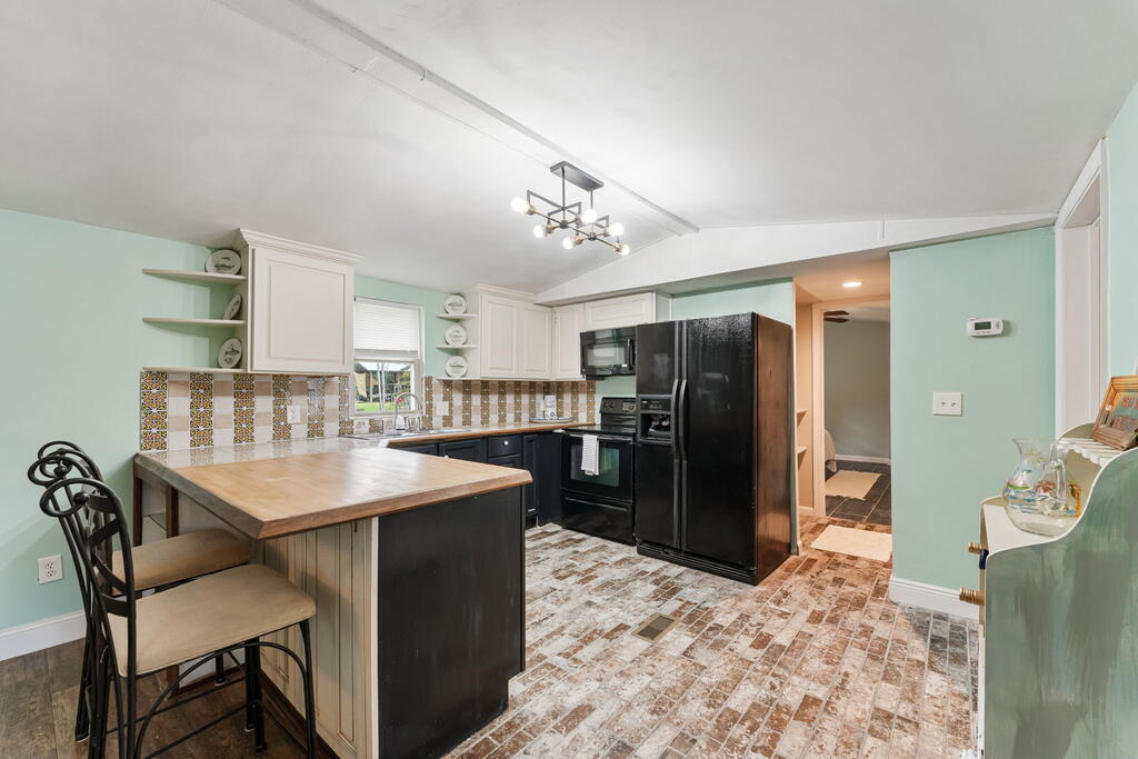 Kitchen with mint-green walls, patterned tile backsplash, black appliances, and a wood-topped island.