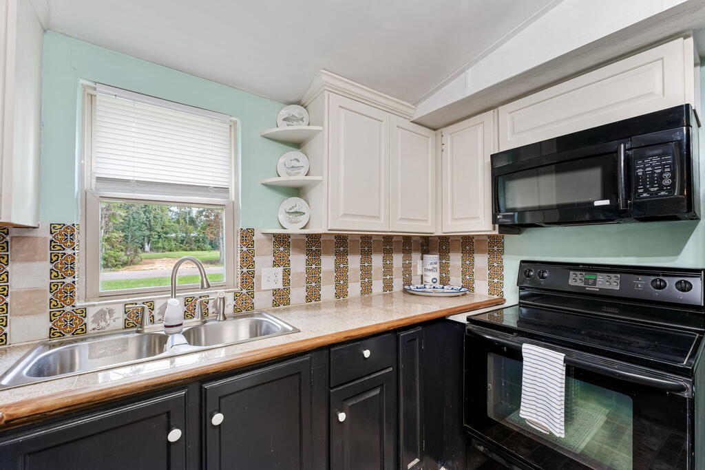 Kitchen with a stainless-steel sink, colorful tile backsplash, and black appliances.