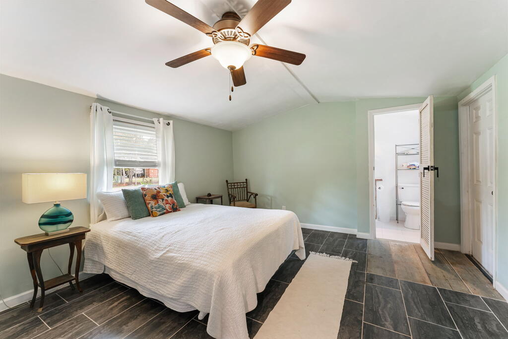 Bedroom with a white bed, pale green walls, dark tile flooring, and an open bathroom doorway.