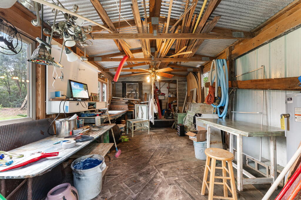 Cluttered workshop with workbenches, tools, and exposed wooden roof framing.