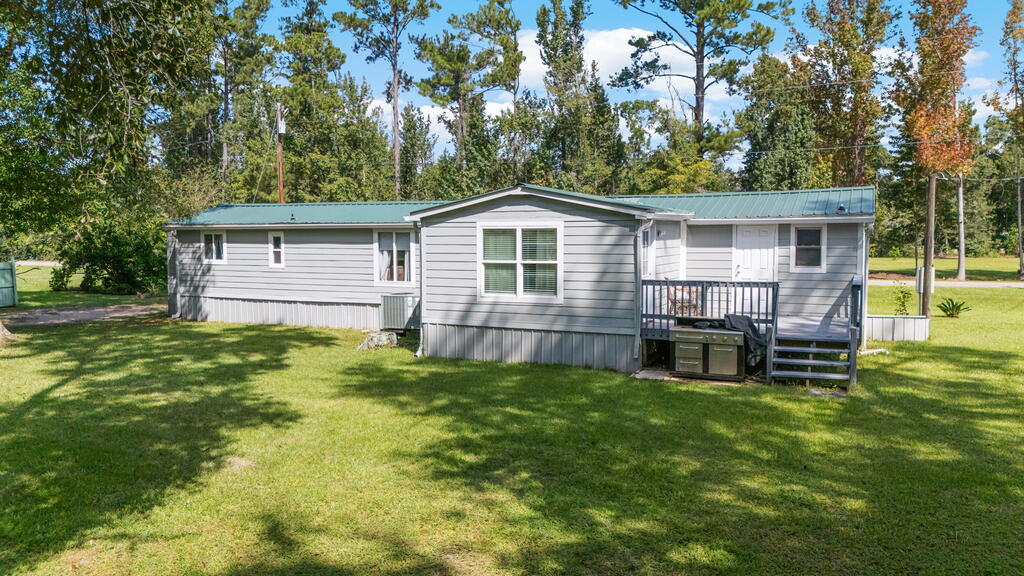 Gray manufactured home with a green metal roof and small porch, set behind a broad lawn.