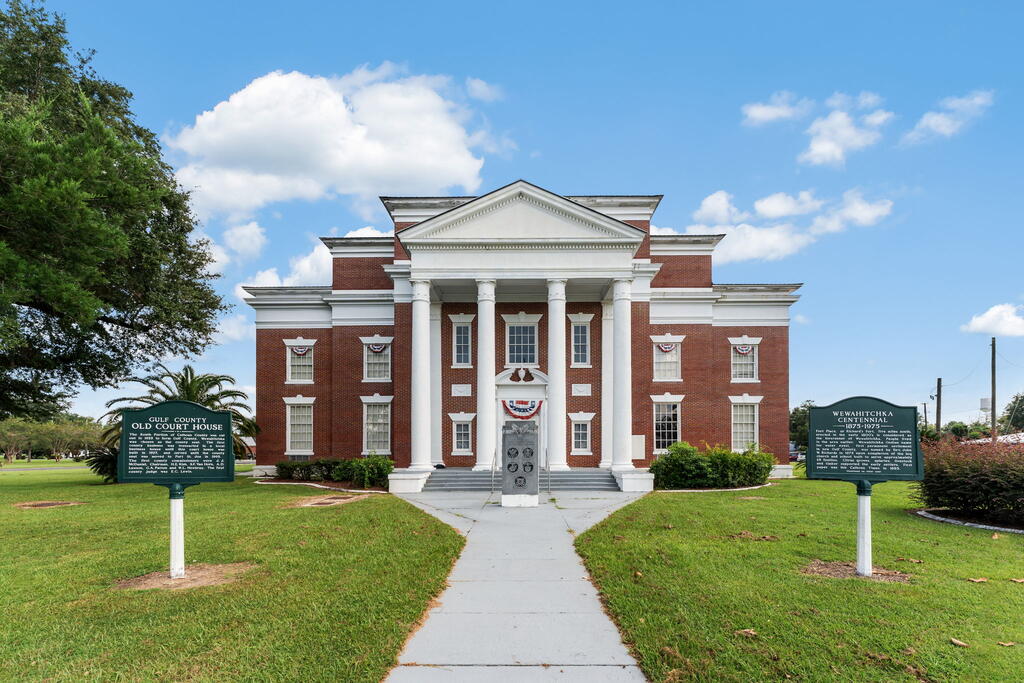 Historic red-brick courthouse with a white columned portico and historical markers on the lawn.