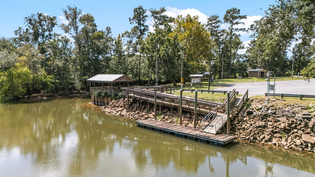 Wooden dock and ramp over a pond beside a covered pavilion and wooded shoreline.