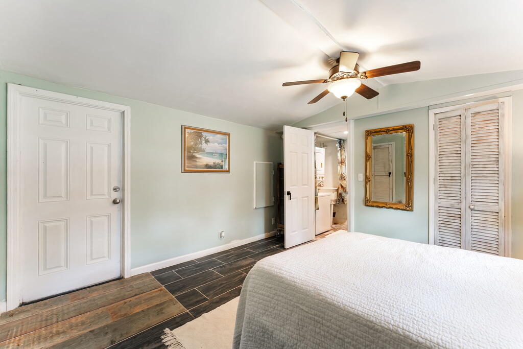 Bedroom with pale green walls, dark tile flooring, a ceiling fan, and louvered closet doors.