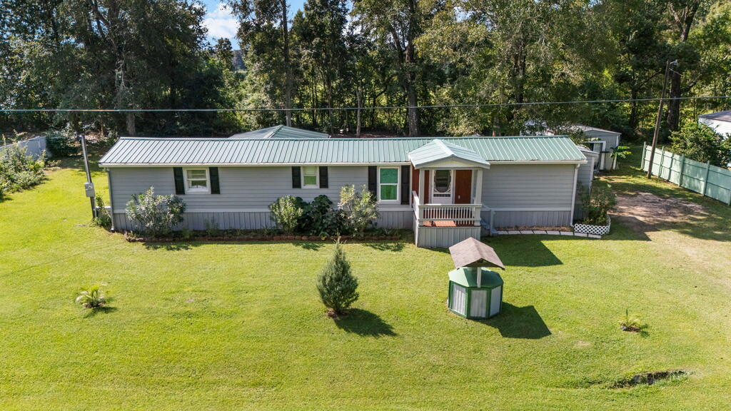 Single-story gray home with a green metal roof, covered porch, and broad front lawn.