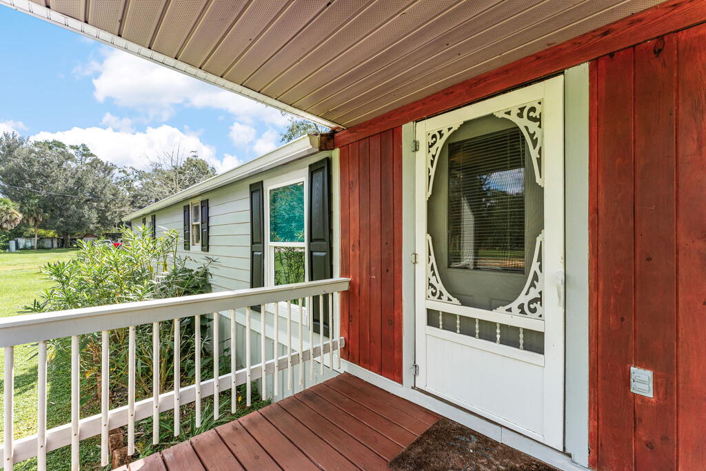 Covered front porch with red siding, decorative white screen door, and white railing.