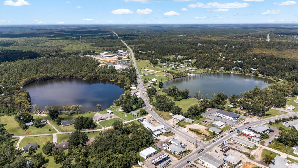 Aerial view of two lakes, scattered buildings, and a road junction amid wooded surroundings.