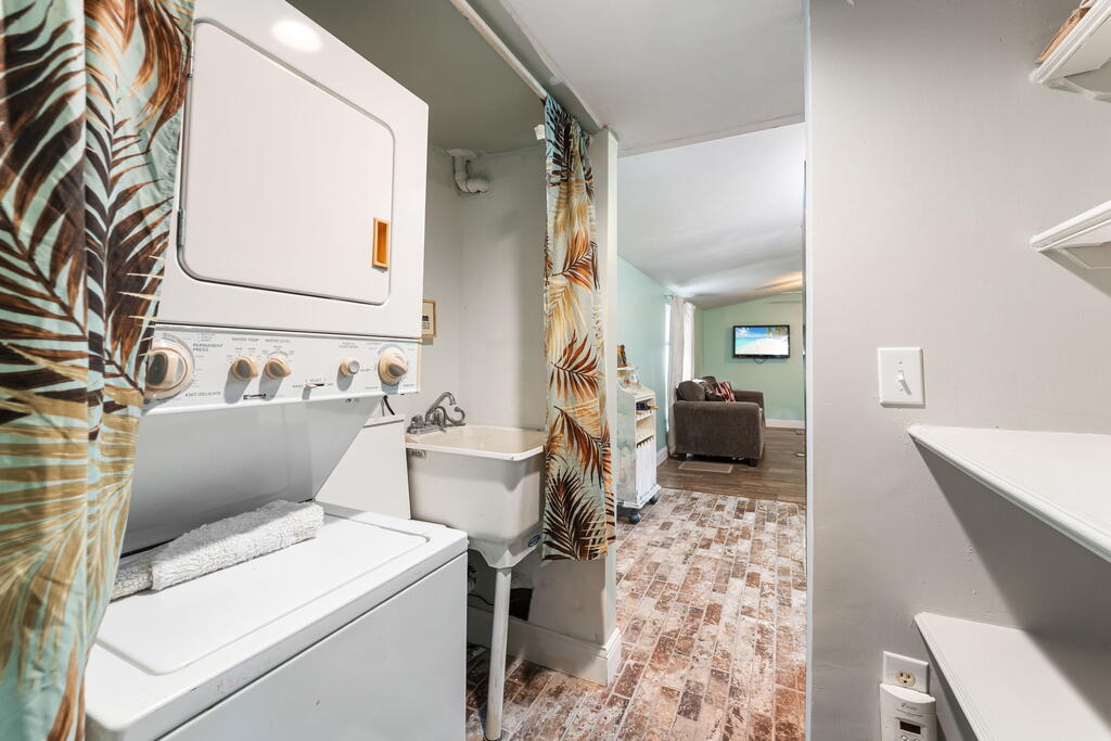 Laundry room with stacked washer and dryer, utility sink, and patterned tile floor.