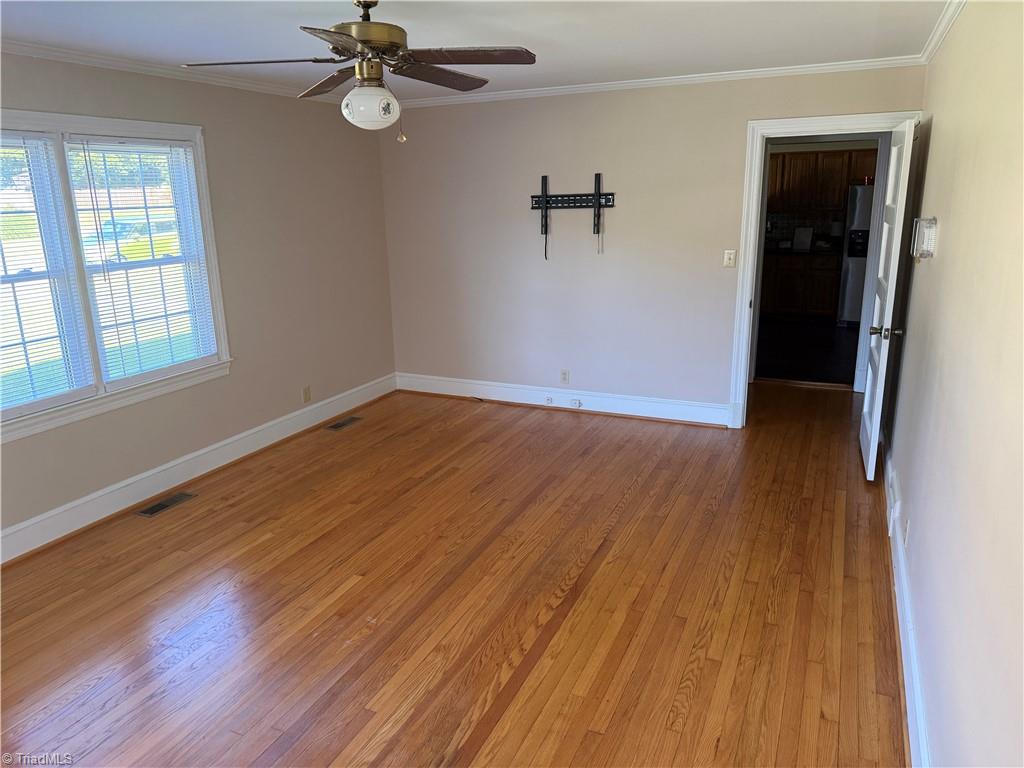 Empty living room with hardwood floors, a ceiling fan, and windows with blinds.
