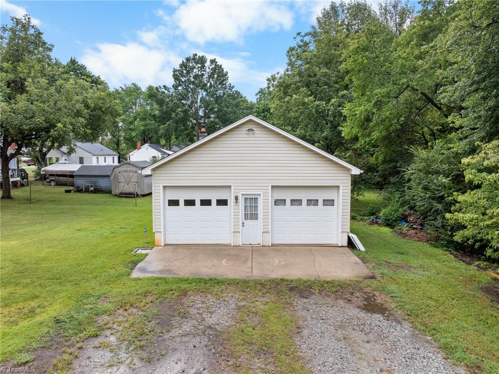 Detached beige two-car garage with a central entry door, concrete apron, and gravel driveway.