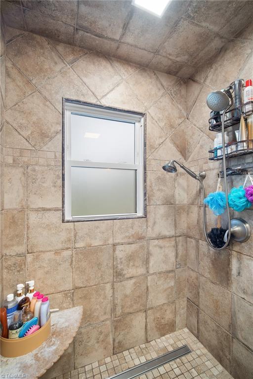 Walk-in shower with tan tile walls, a frosted window, and a handheld showerhead.