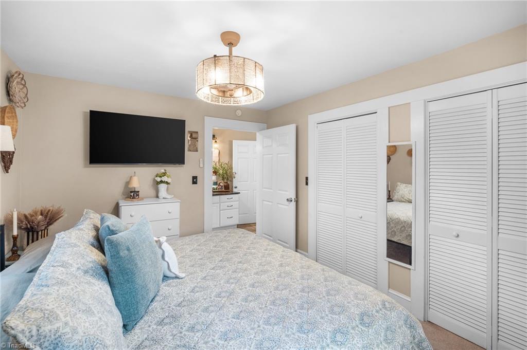 Bedroom with blue patterned bedding, a wall-mounted television, dresser, and white louvered closet doors.