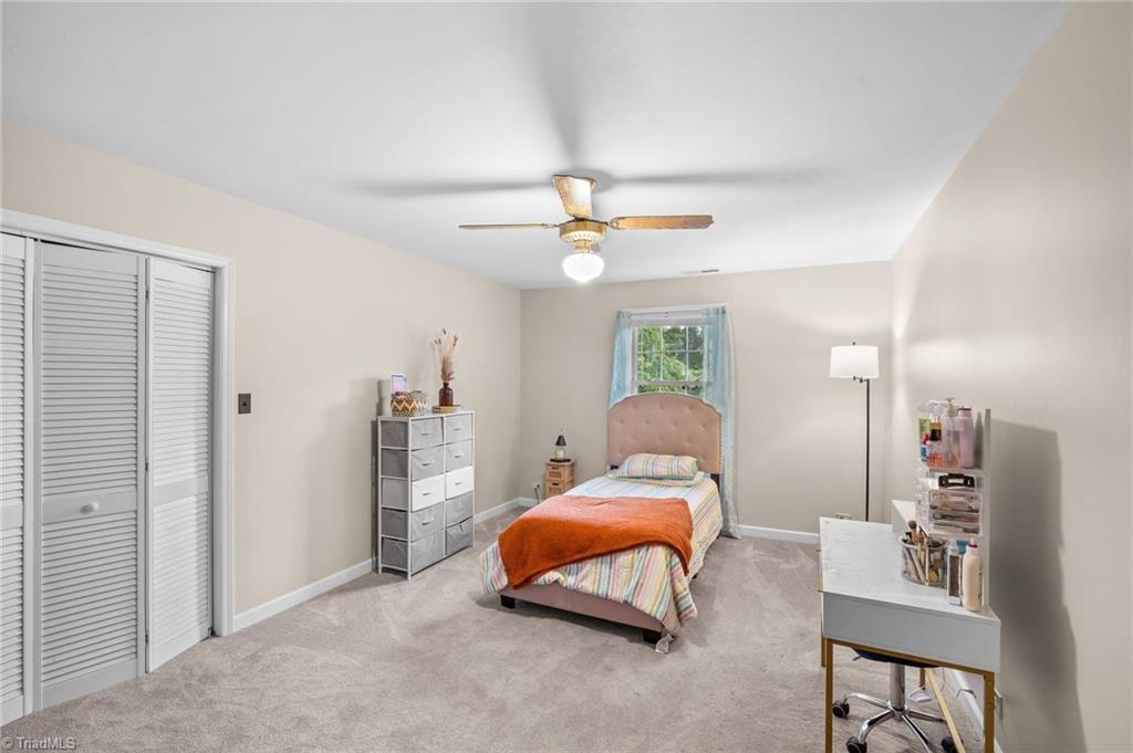 Furnished bedroom with a single bed beneath a window with blue curtains and a ceiling fan.