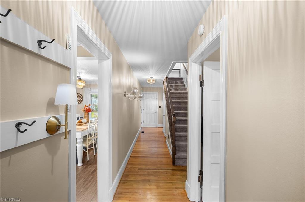 Hallway with hardwood floors, coat hooks, and a carpeted staircase beside an open dining-room doorway.