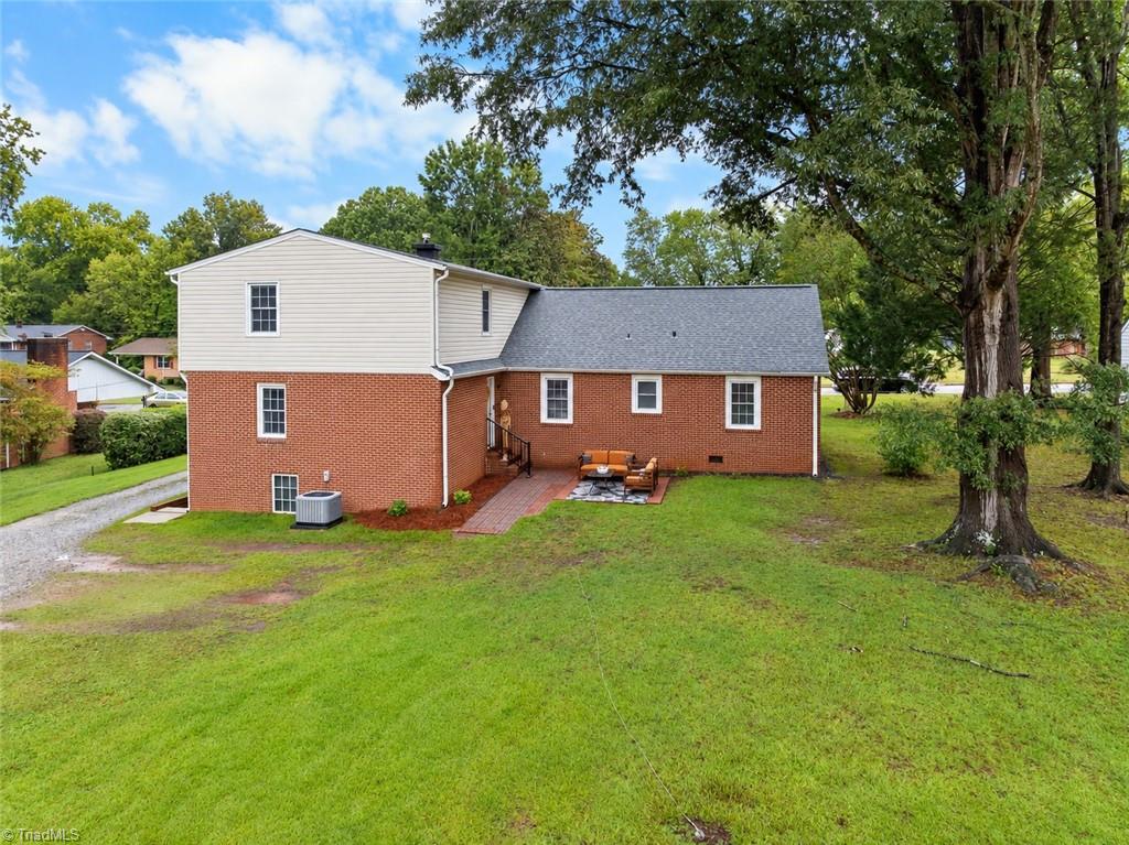 Rear of a two-story brick-and-siding home with a patio, lawn, and mature trees.