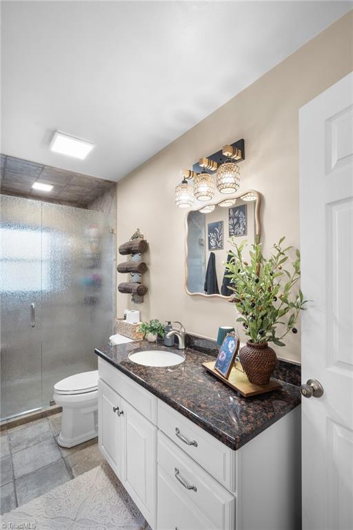Bathroom with a dark stone vanity, glass-enclosed shower, and decorative mirror.
