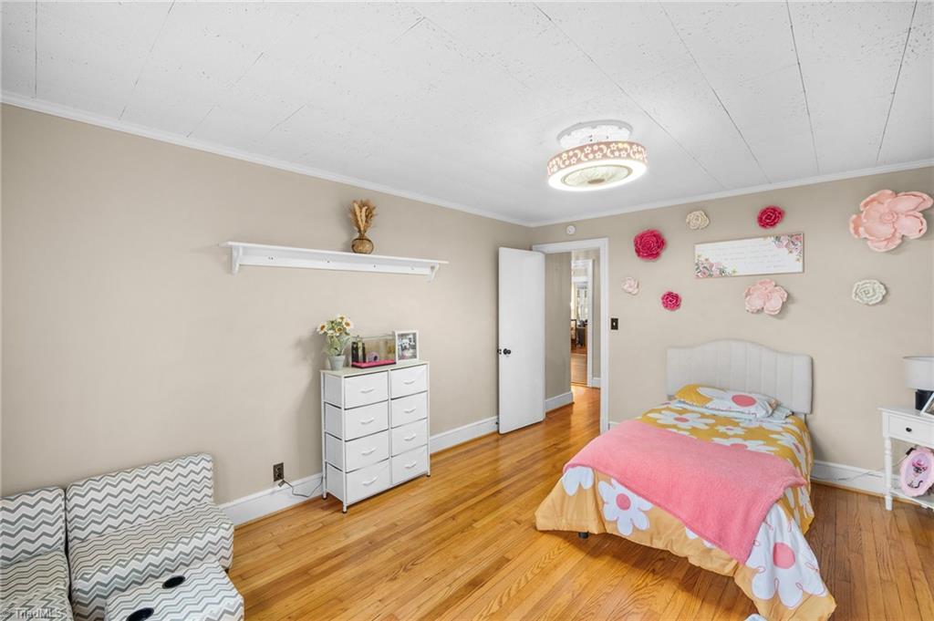 Bedroom with colorful floral bedding, hardwood floors, a white dresser, and a chevron-patterned chair.